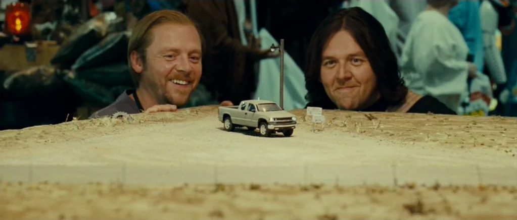 Paul (2011) movie still: medium — Two men stand behind a large scale-model landscape of a desert road. The men gaze down at a miniature pickup truck…