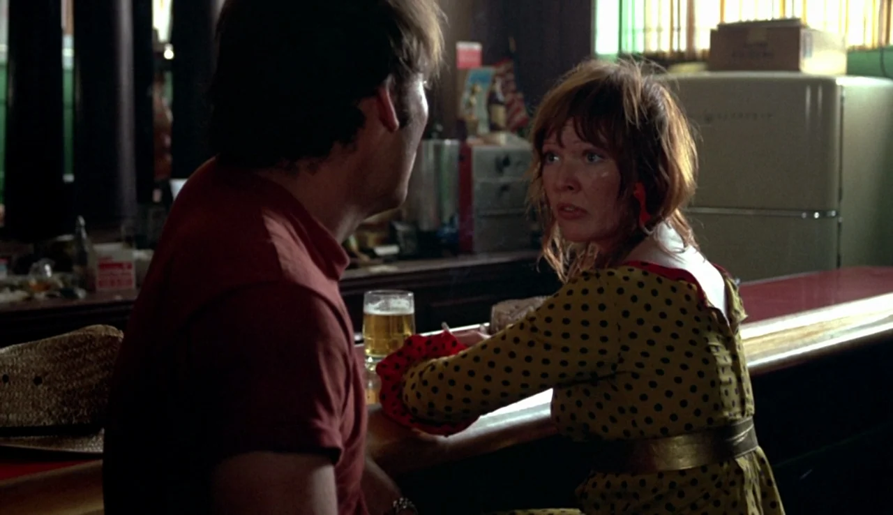 Fat City (1972) movie still: medium — A dimly lit bar interior featuring a refrigerator and miscellaneous bar supplies in back. A man and a woman…