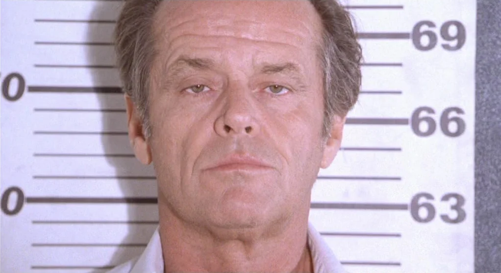 The Crossing Guard (1995) movie still: closeup — A white mugshot backdrop displays height markers in increments from sixty-three to sixty-nine…
