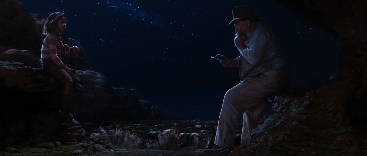 Australia (2008) movie still: wide — A rugged desert landscape under a clear, starry night sky. An elderly man and a young girl sit on opposite…