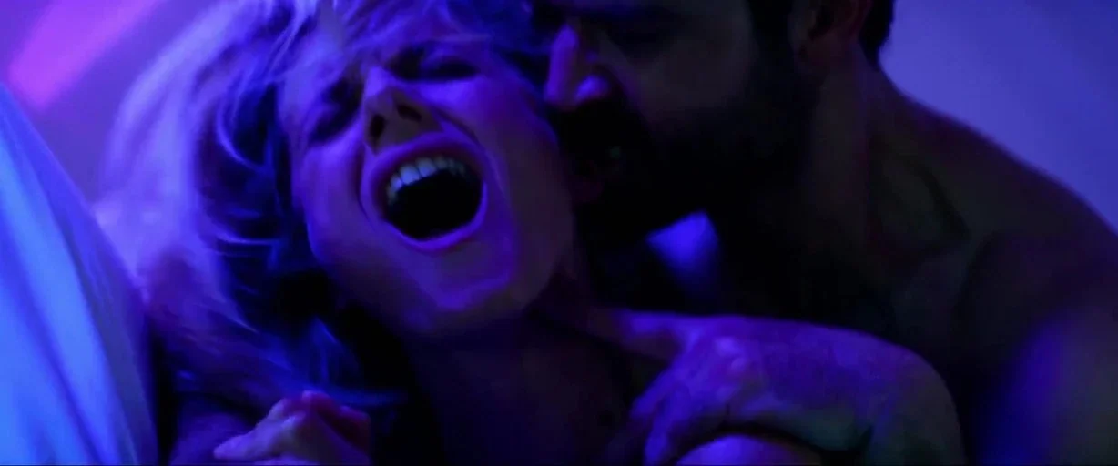 6 Underground (2019) movie still: closeup — A close-up of a man and woman in a dimly lit, blue-hued room. The man kisses the woman's neck as her…