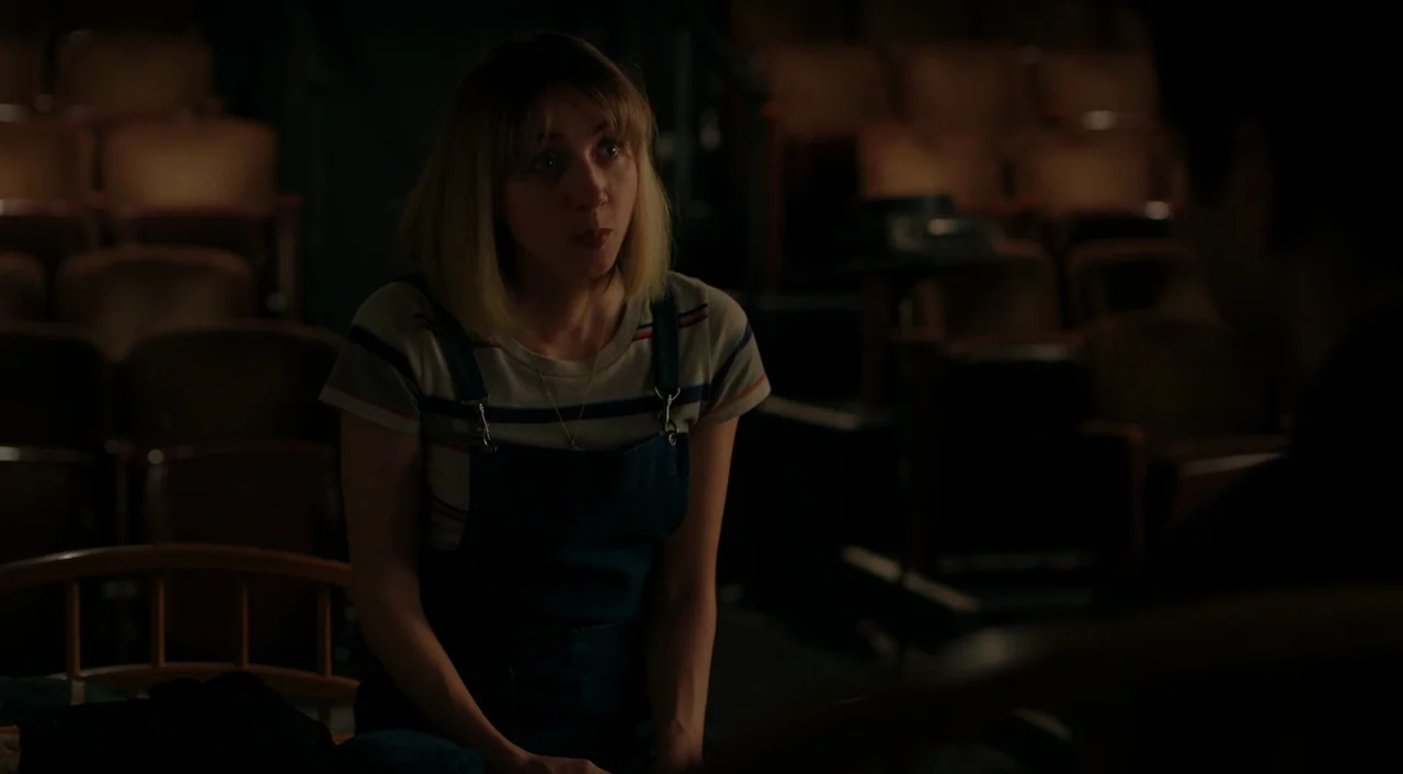 The Big Sick (2017) movie still: medium — A dark, empty space featuring rows of faded brown velvet seating in a theater. A young woman sits in the…