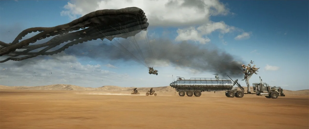 Furiosa: A Mad Max Saga (2024) movie still: wide — A vast, flat desert landscape stretches under a bright blue sky with scattered clouds. A chrome…