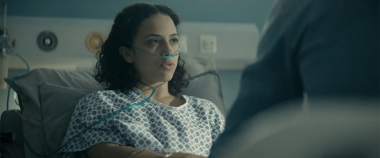 Perfect Addiction (2023) movie still: medium — A hospital room features medical equipment mounted on a pale blue wall. A woman in a hospital gown…