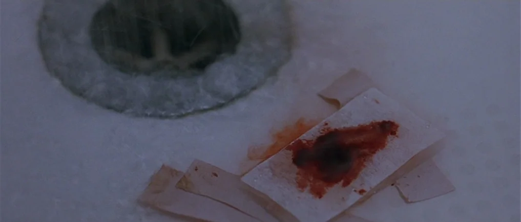 Sexy Beast (2000) movie still: closeup — A white ceramic sink basin features a metallic drain and a soiled adhesive strip. A blood-stained bandage…