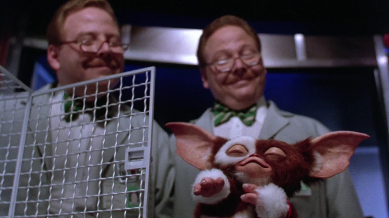 Gremlins 2: The New Batch movie still: medium — A man in a lab coat stands behind a creature in a scientific facility. The man holds the small brown…