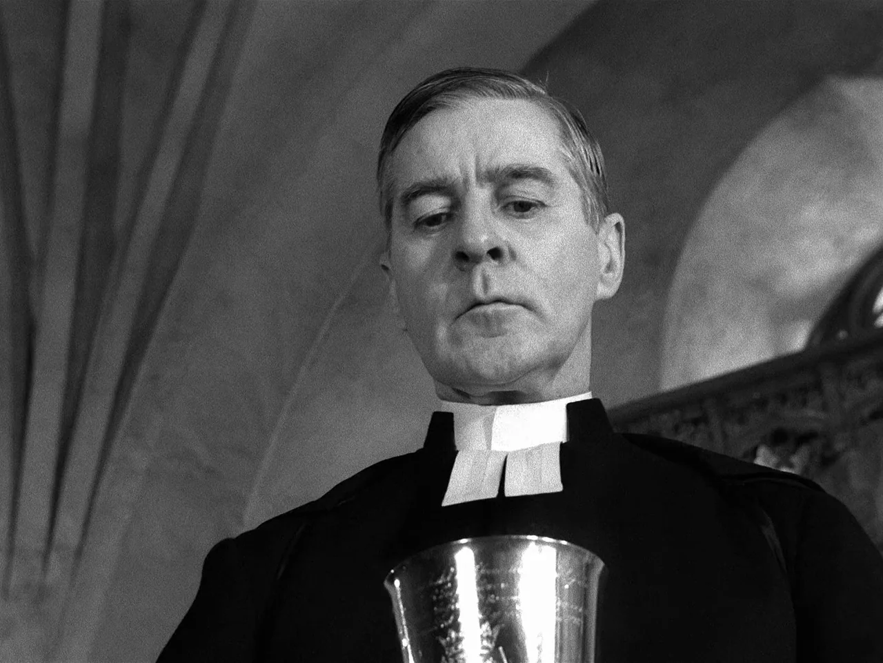 Winter Light (1963) movie still: medium — A stone interior with vaulted ceilings provides the background for a religious ceremony. A priest wearing…