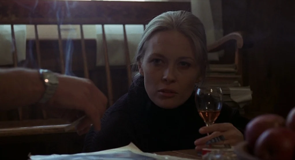 Puzzle of a Downfall Child (1970) movie still: medium — A dimly lit room with a wooden chair and apples on a table. A woman watches a hand hold a…