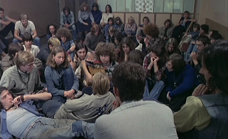 Blind Chance (1987) movie still: wide — A crowded, large indoor hall filled with many young people sitting on the floor. The individuals are…