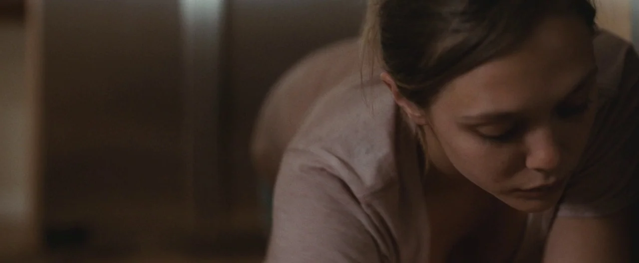 Martha Marcy May Marlene (2011) movie still: closeup — A dimly lit room with soft textures and muted earth-tone walls. A young woman leans toward…