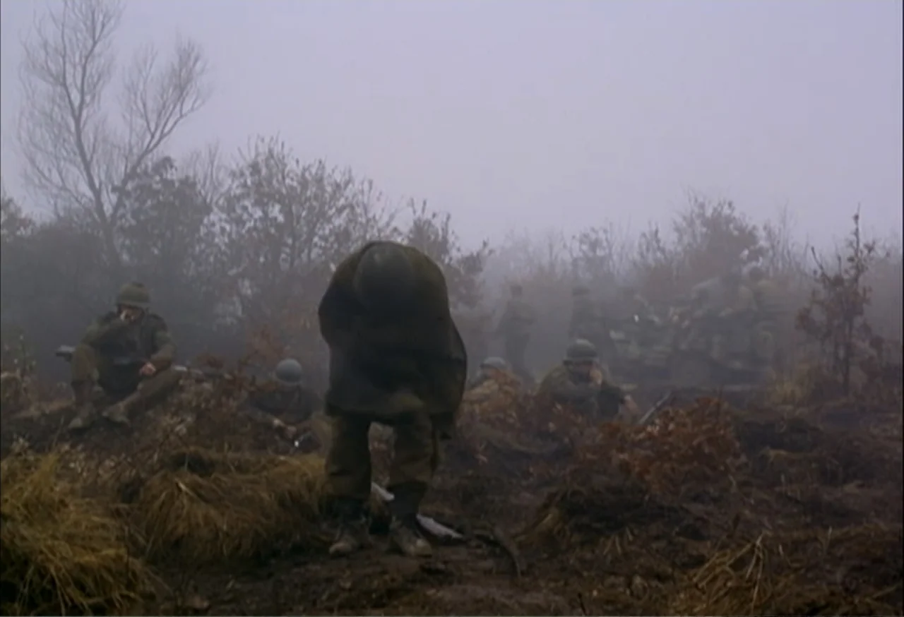 When Trumpets Fade (1998) movie still: medium — A muddy, fog-covered landscape features sparse leafless trees and a group of soldiers. A central…