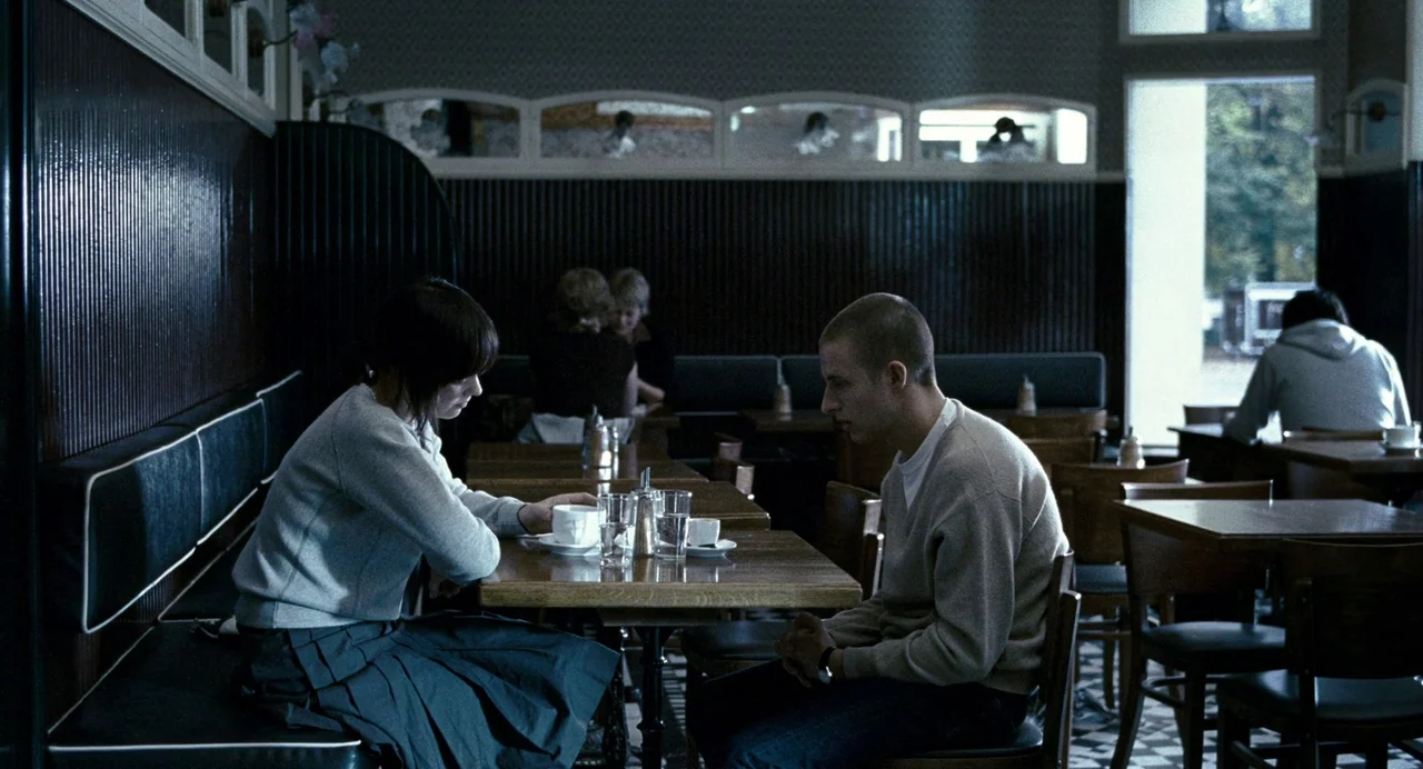 Reprise (2006) movie still: medium — A quiet diner interior features wood paneling and tiled floors under dim lighting. A young man and woman sit…