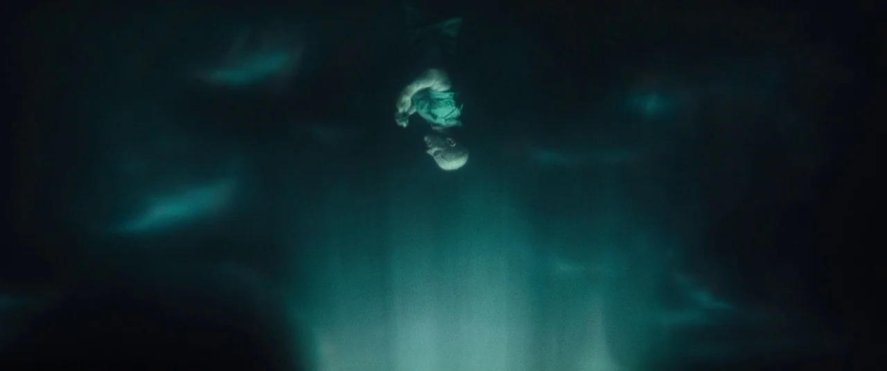Deadpool 2 (2018) movie still: wide — A dark, murky expanse of water is illuminated by a faint teal light source. A lone man sinks vertically…