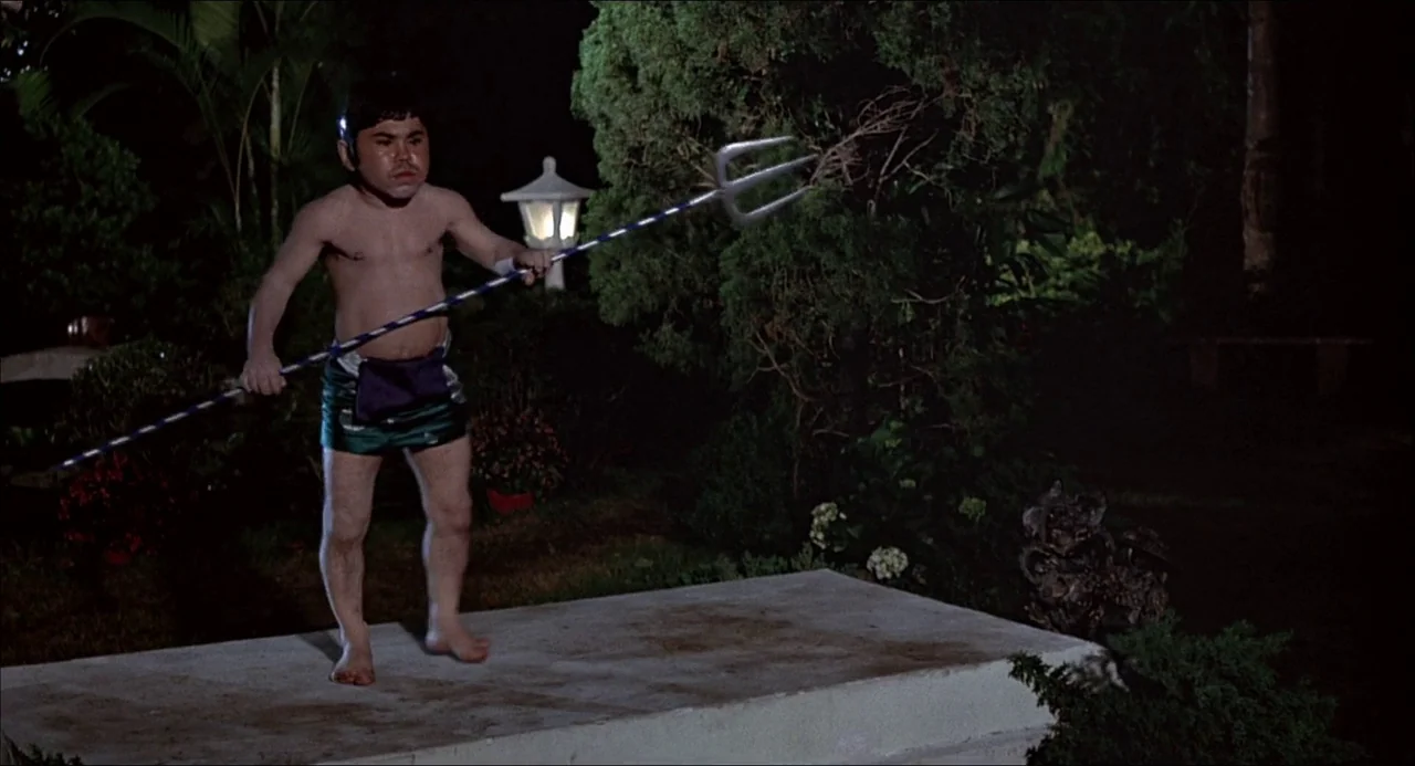 The Man With the Golden Gun (1974) movie still: fullbody — A nighttime outdoor setting features lush shrubs and a small concrete platform. A…