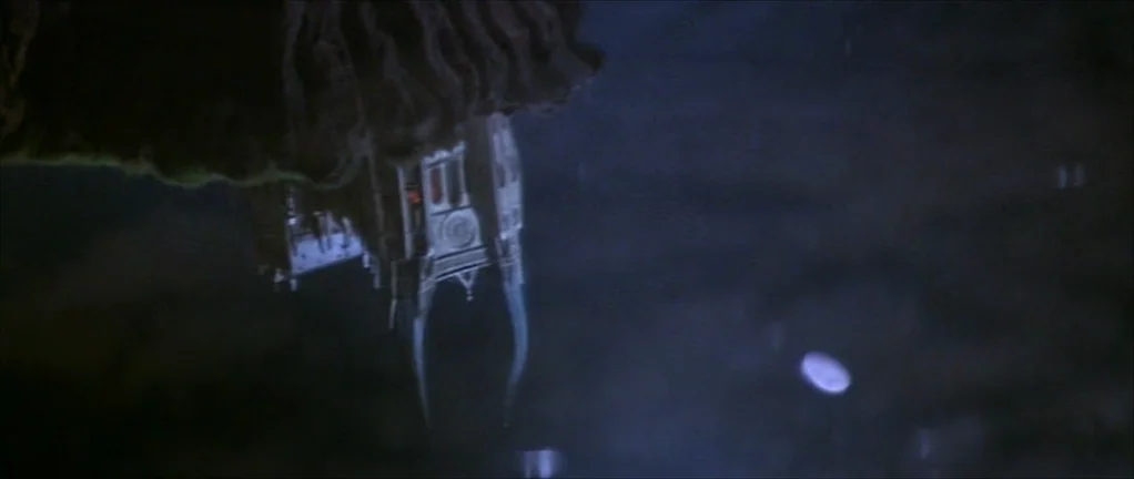 The Moon in the Gutter (1983) movie still: wide — An upside-down reflection of a large gothic building appears on the water surface. Dark water…