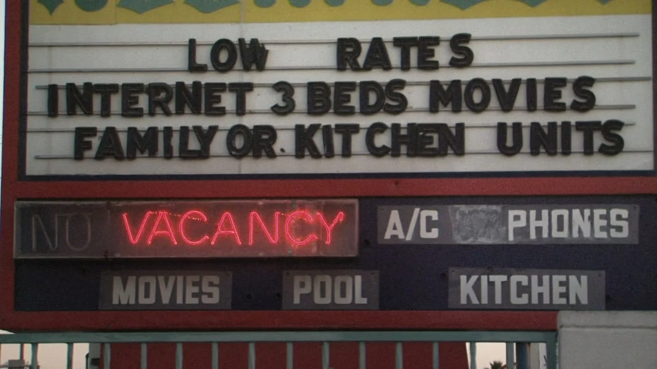 Homeless: The Motel Kids of Orange County (2010) movie still: establishing — A roadside motel sign displays list of amenities and vacancies in black…