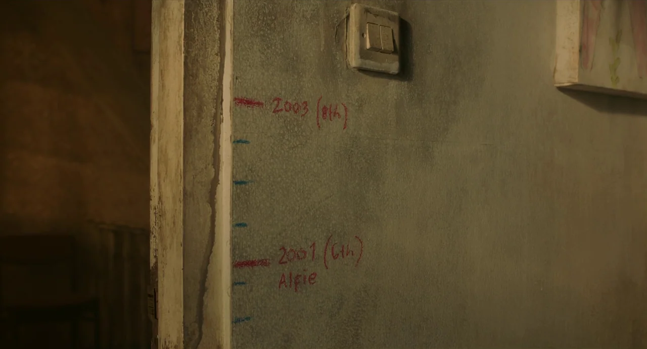 May The Devil Take You (2018) movie still: closeup — A weathered gray wall adjacent to a door frame features hand-drawn height measurements. Red…