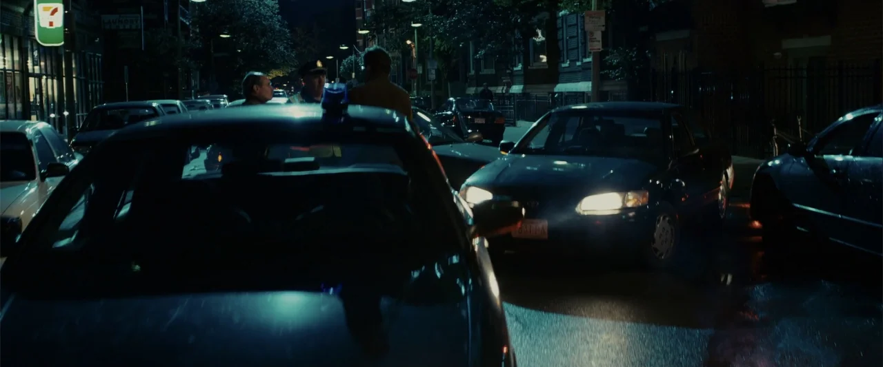Zookeeper (2011) movie still: medium — An urban parking area at night features multiple parked sedans and street lighting. Three people stand…