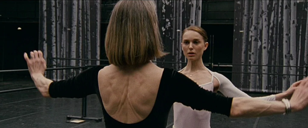 Black Swan (2010) movie still: medium — A spacious dance rehearsal room features tall black and white curtains depicting birch trees. Two ballerinas…