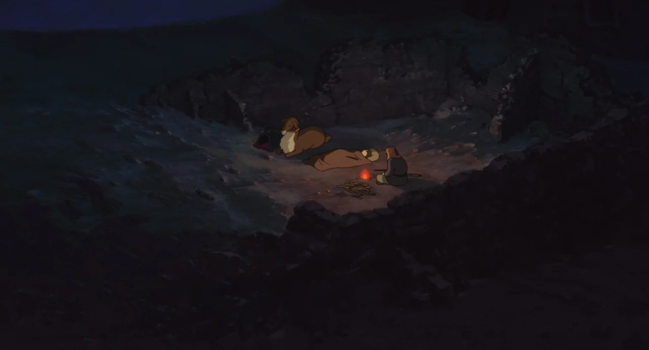 Tales From Earthsea (2006) movie still: wide — The interior of stone ruins at night with a small campfire flickering on the ground. A person sits…
