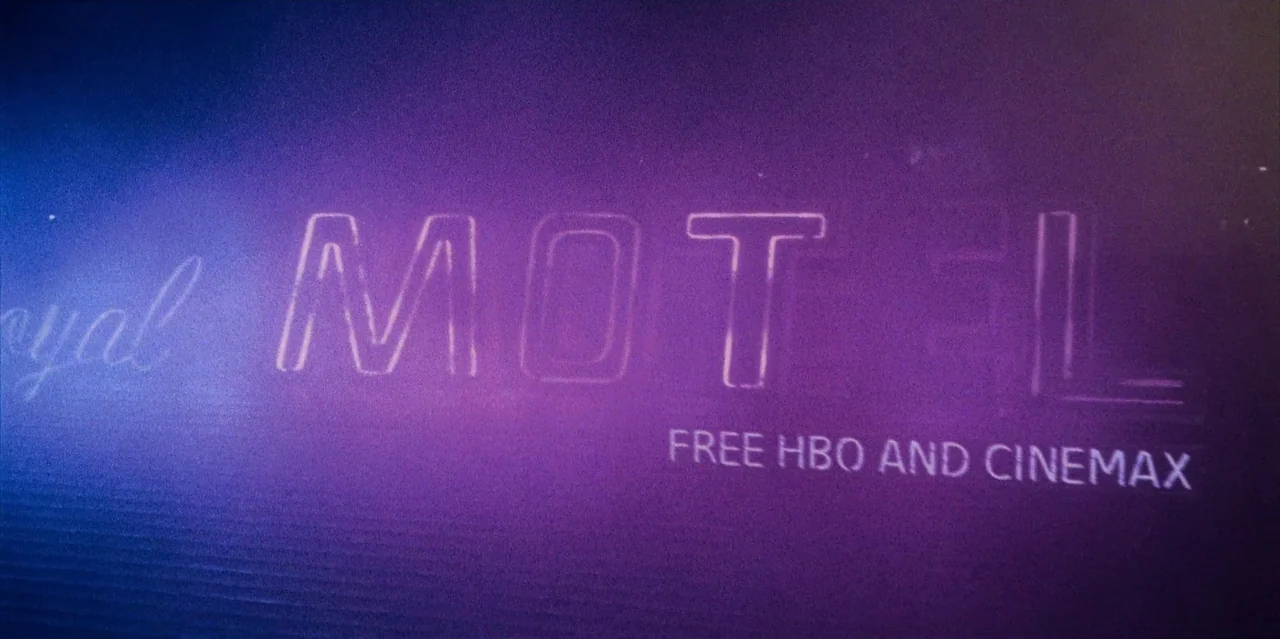 They Cloned Tyrone (2023) movie still: closeup — A close-up of a dark purple neon sign for a motel at night. The sign features the words royal motel…