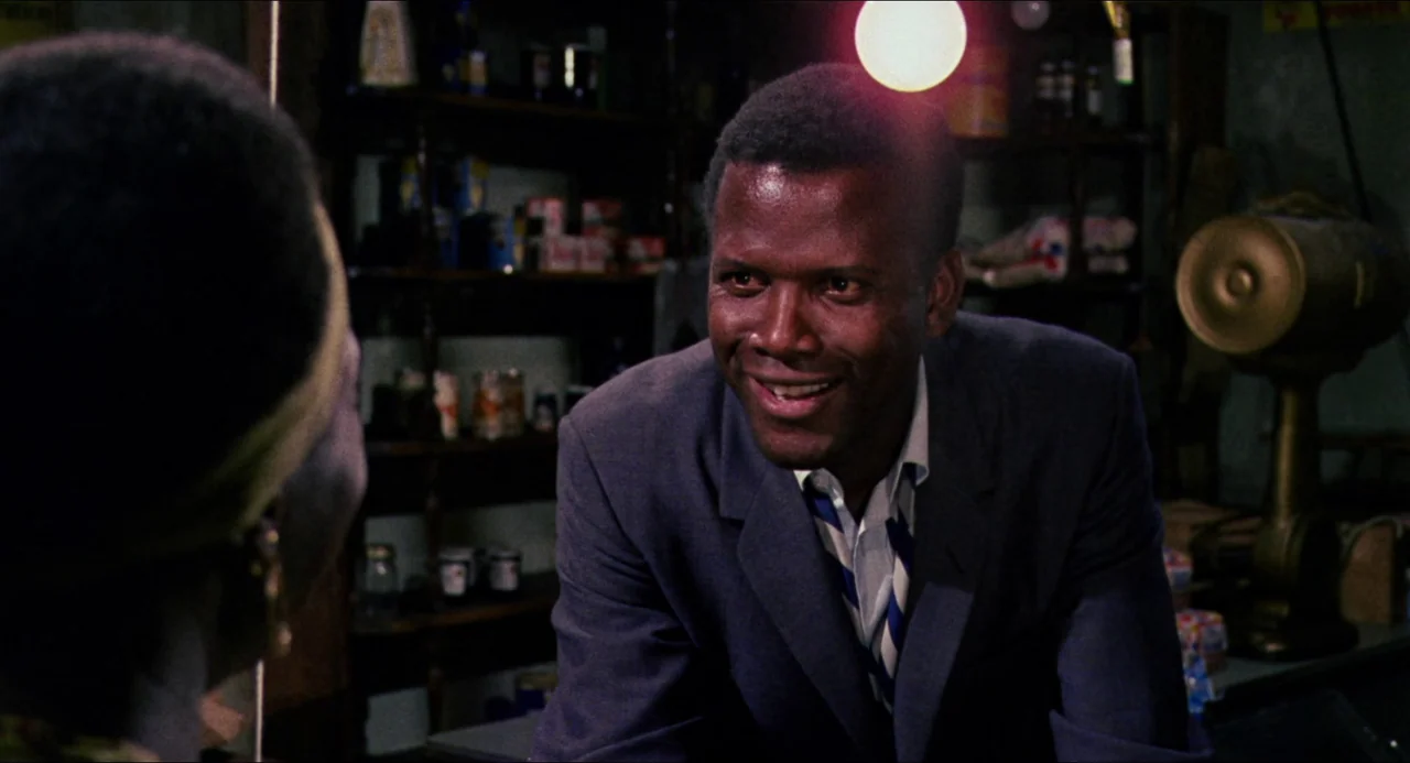 In the Heat of the Night (1967) movie still: medium — A small retail space with dark wooden shelving units holding various packaged food items. A…