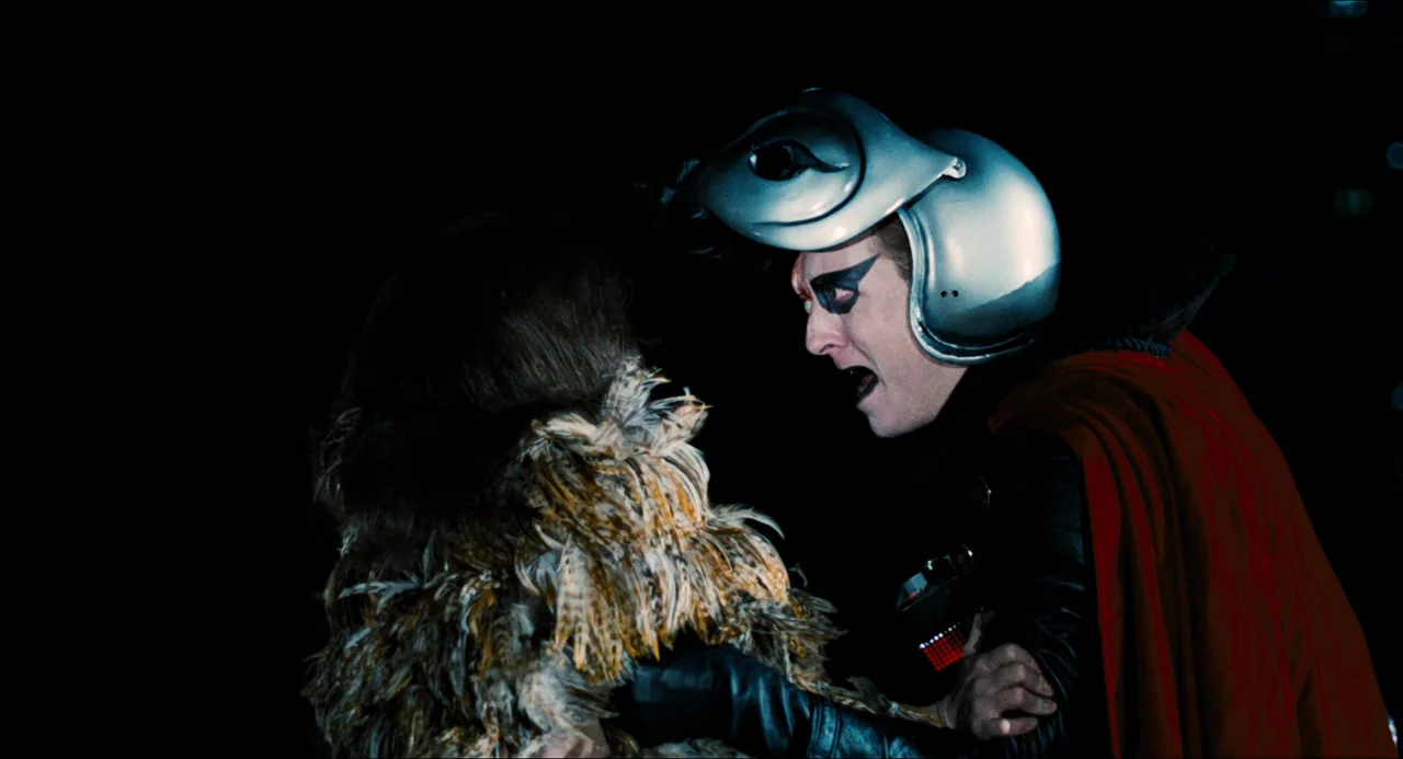 Phantom of the Paradise (1974) movie still: medium — Two individuals stand against a pitch-black background. A man wearing a futuristic helmet…
