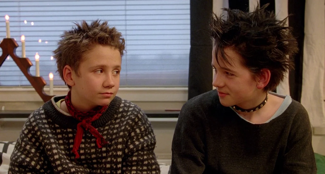 We Are The Best! (2013) movie still: medium — Two teenagers with spiked hair sit in a room in front of a window. One boy wears a patterned sweater…