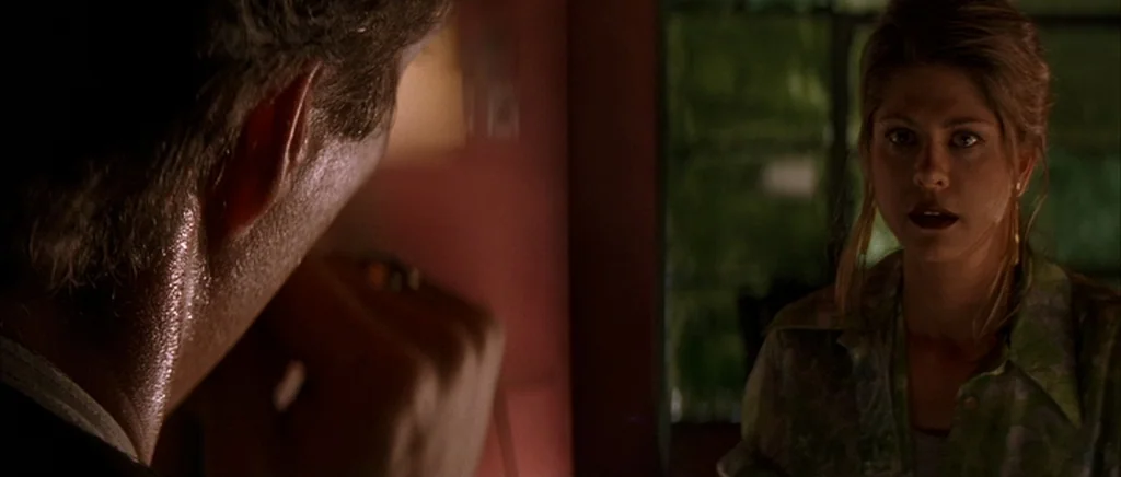 The Underneath (1995) movie still: medium — A dimly lit room with a deep red wall and a dark window frame. Two people converse while facing each…