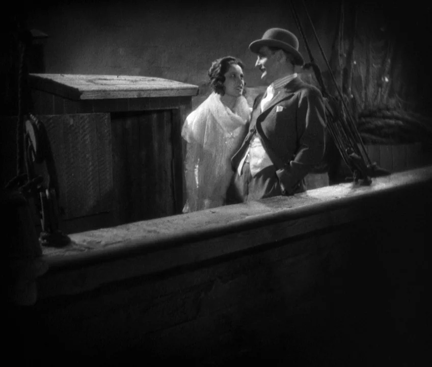 The Threepenny Opera (1931) movie still: medium — A dark night on a ship deck with wooden railings and rope equipment visible. A man in a suit and…