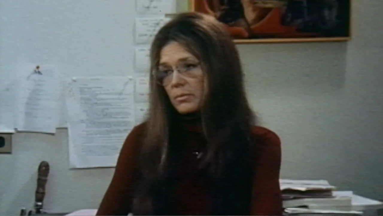 Dear Ms.: A Revolution in Print (2025) movie still: medium — A 1970s office interior features plain grey walls decorated with pinned papers and a…