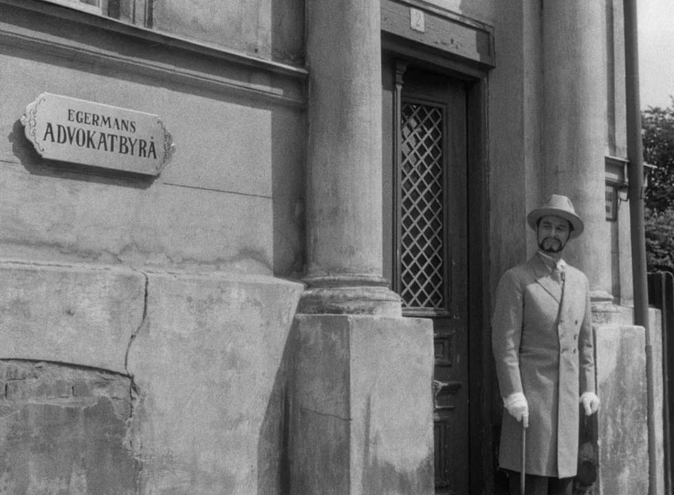 Smiles Of A Summer Night (1955) movie still: medium — A weathered stone building features a doorway and a sign labeled Egermans Advokatbyrå. A man…