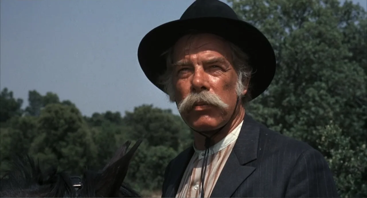 The Spikes Gang (1974) movie still: medium — An older man sits atop a horse against a backdrop of blurry green trees. He wears a formal suit and hat…
