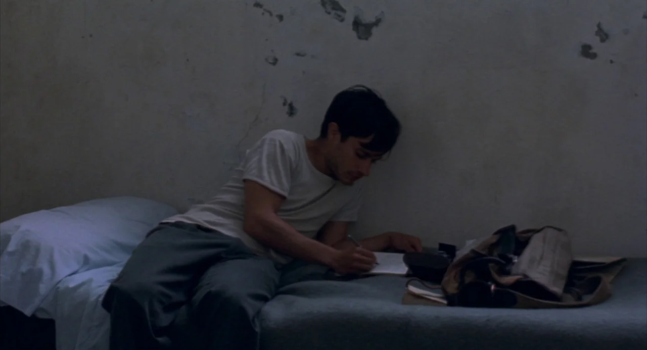 The Motorcycle Diaries (2004) movie still: medium — A spartan room features concrete walls with patches of peeling paint and a narrow bed. A young…