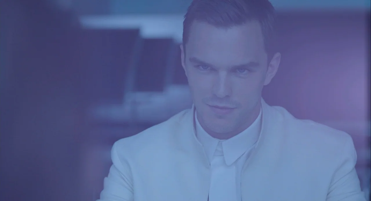 Equals (2015) movie still: medium — A minimalist, brightly lit interior office space with blurred workstation monitors in the background. A young…