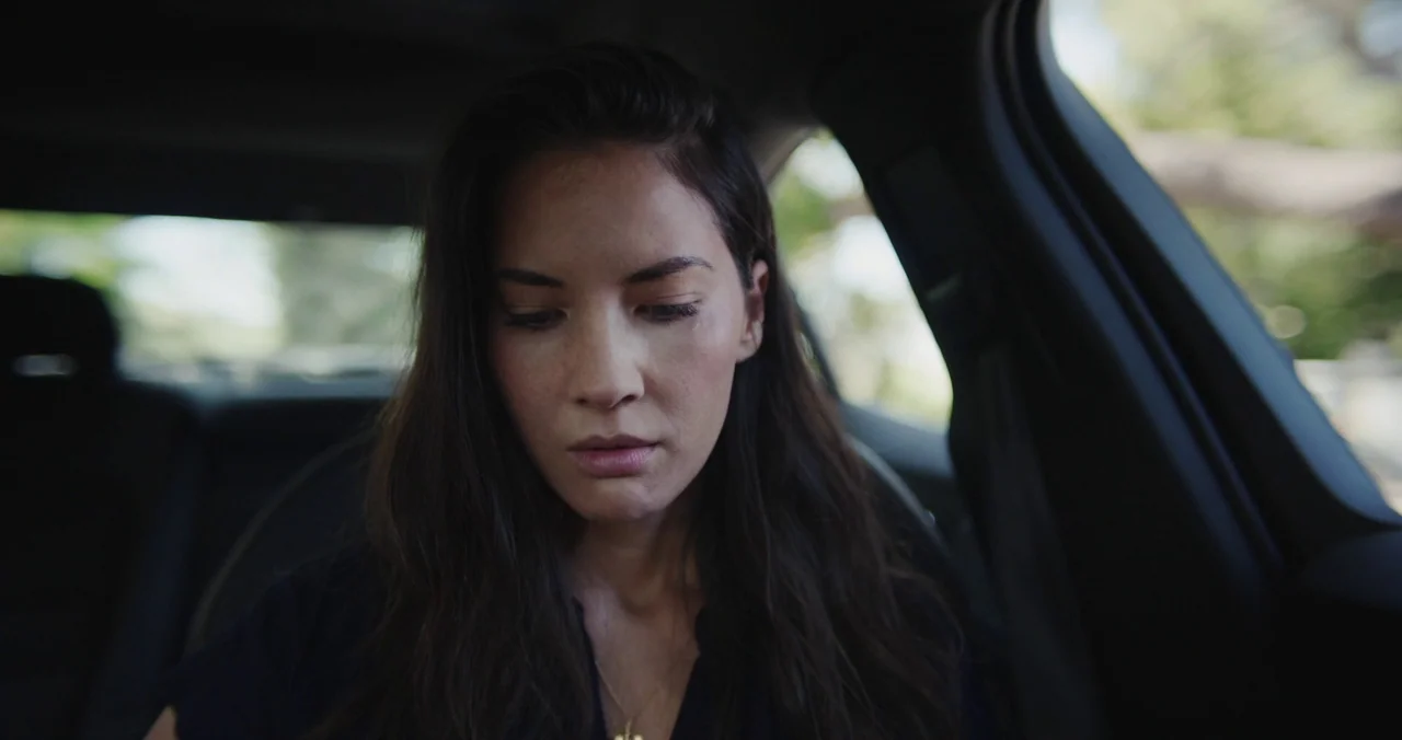 Violet (2021) (2021) movie still: closeup — The interior of a moving vehicle with a blurred background visible through the window. A woman with long…
