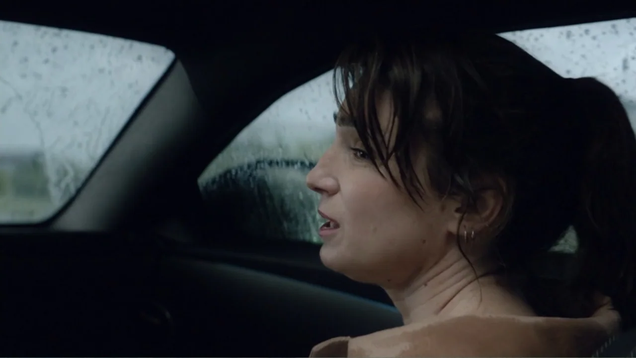 I Married a Dumbass (2016) movie still: closeup — Inside a parked car during rain, the view is directed toward the side window. A woman looks out…