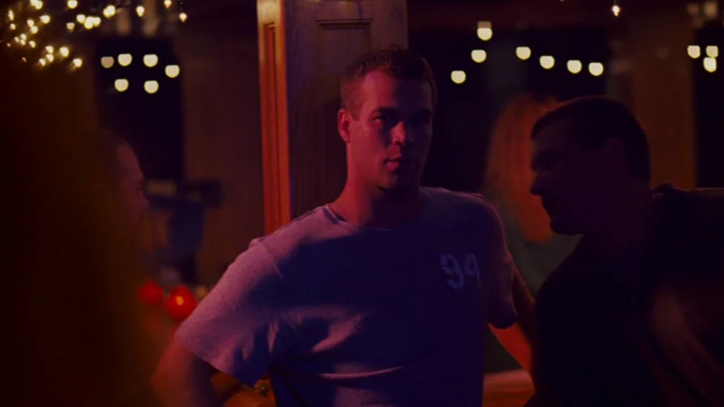 Sugar (2008) movie still: medium — A dimly lit bar environment features warm red accents and blurred background fairy lights. A man in a grey…