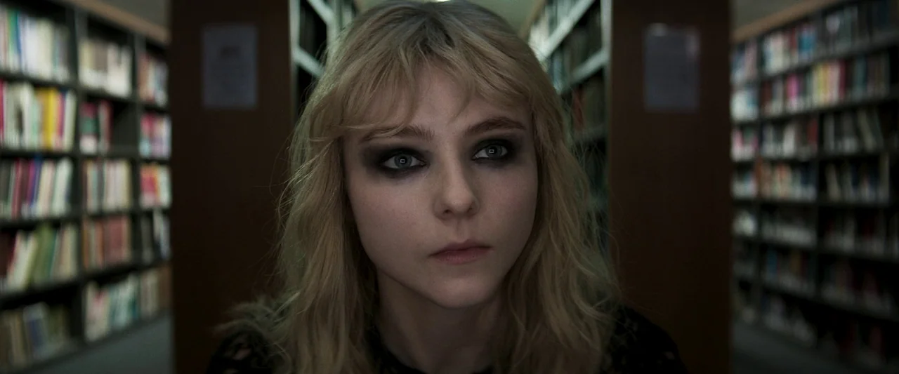 Last Night in Soho (2021) movie still: closeup — A woman stands between two tall shelves filled with colorful books. She looks directly forward into…