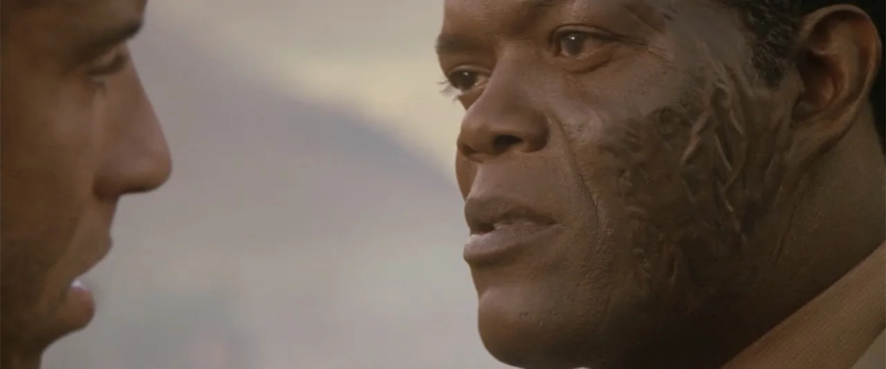 xXx (2002) movie still: closeup — An outdoor area with a blurred background under warm golden lighting. A man with facial scarring looks toward…