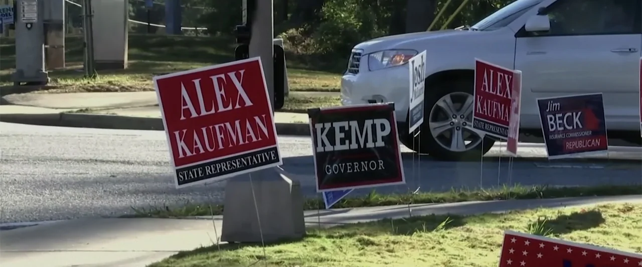 All In: The Fight for Democracy (2020) movie still: medium — A row of political campaign signs is staked into the grass by a paved road. A white SUV…