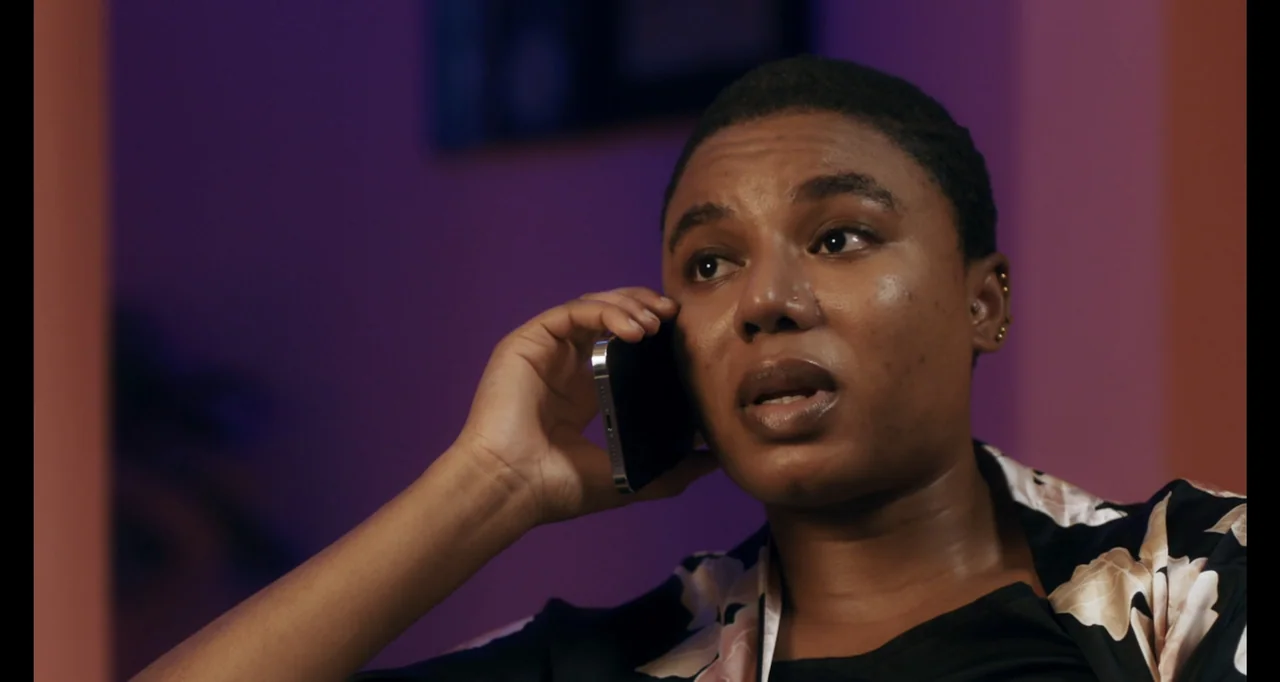 Love In A Pandemic (2023) movie still: closeup — A dimly lit indoor space with purple and pink walls. A young woman talks on her mobile phone.