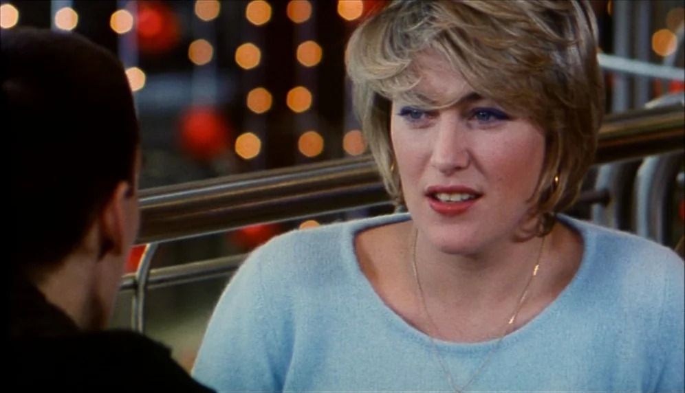 Nenette et Boni (1996) movie still: medium — A woman speaks to another person in a dimly lit restaurant at night. Numerous out-of-focus lights…