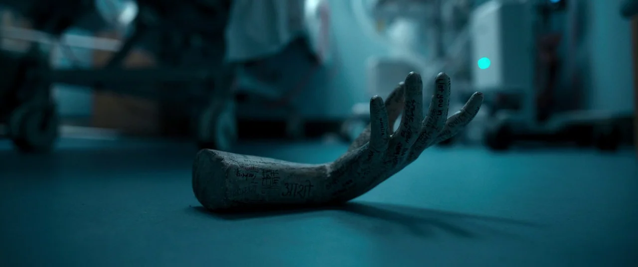 Talk To Me (2022) movie still: closeup — A pale, carved plaster hand lies on the linoleum floor of a medical facility. The object is covered in…