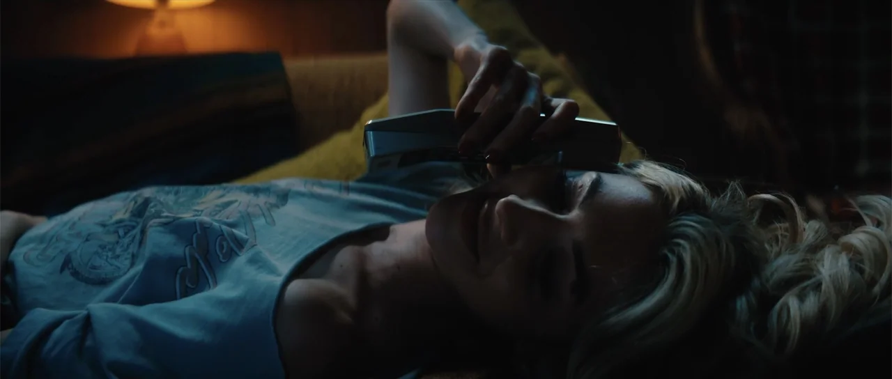 Night of the Missing (2023) movie still: medium — A dimly lit room contains a couch where a woman rests during the evening. She lies down on the…