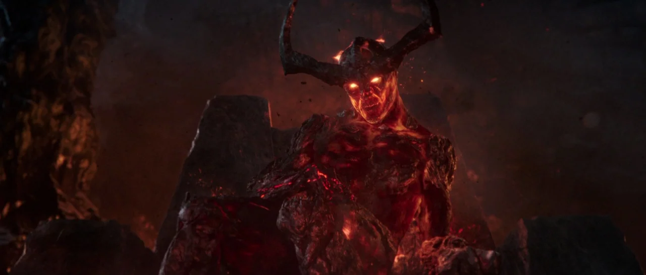 Thor: Ragnarok (2017) movie still: medium — A dark, cavernous space with a rough, jagged stone throne. A demonic entity with glowing red skin sits…