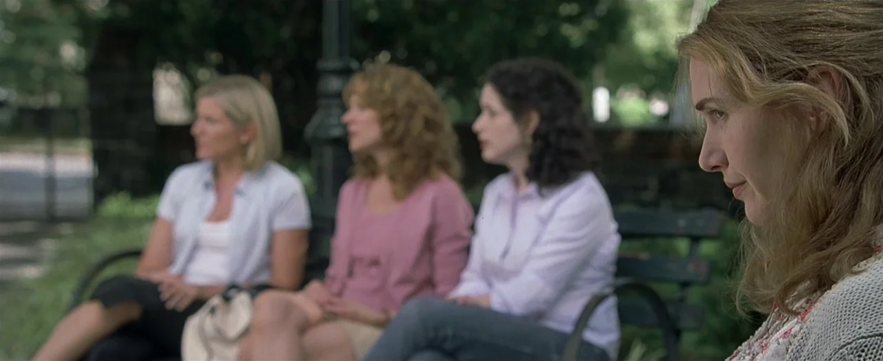 Little Children (2006) movie still: medium — A green park bench holds three women while another woman sits in the foreground. They are located…