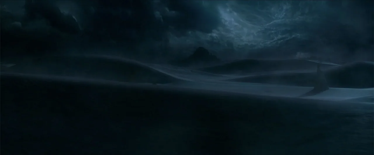 Monster Hunter (2020) movie still: establishing — A vast, undulating expanse of sand dunes sits under a heavy, storm-filled night sky. Dark,…