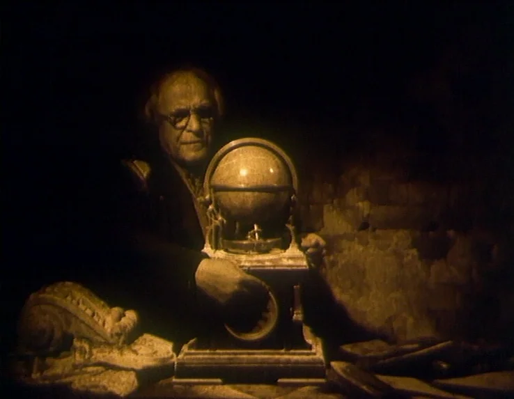 Dead Man’s Letters (1986) movie still: medium — A dimly lit room with stone walls and scattered debris in the background. An elderly man in a dark…