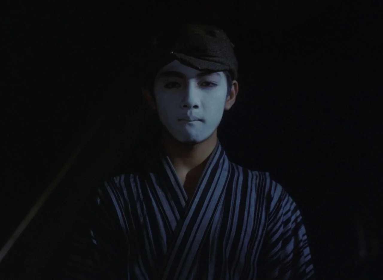Pastoral To Die In The Country (1974) movie still: medium — A person stands against a pitch black background in minimal lighting. The subject is…